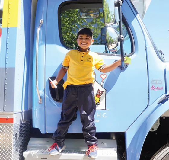 young hispanic boy standing on side step of the care mobile, holding onto side mirror and smiling